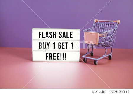 Flash Sale Buy 1 Get 1 Free text on LED lightbox with trolley shopping cart on pink and purple geometric background 127605551