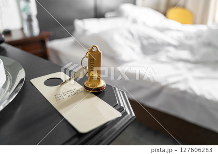 A hotel room key sits on the nightstand with a comfortable bed situated in the background A hotel room key sits on the nightstand with a comfortable bed situated in the background 127606283