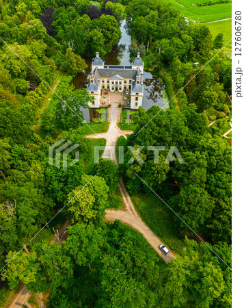 Aerial view of a historic castle surrounded by a forest, with vast green fields, winding waterways, and a river stretching across the flat Dutch countryside under a partly cloudy sky. 127606780