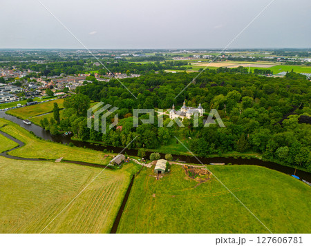 Aerial view of a historic castle surrounded by a forest, with vast green fields, winding waterways, and a river stretching across the flat Dutch countryside under a partly cloudy sky. 127606781