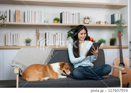Digital Engagement and Pet Love. Woman using tablet with her corgi dog by her side at home. 127607959