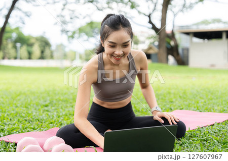 Yoga and technology. A woman engages in yoga practice while using a laptop outdoors. Yoga and technology. A woman engages in yoga practice while using a laptop outdoors. 127607967