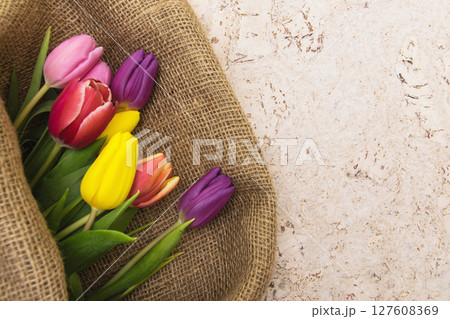 Multicolor tulips bouquet in natural fabric wrapping paper. Spring flowers on the cork background . Top view with place for text. Copy space. Multicolor tulips bouquet in natural fabric wrapping paper. Spring flowers on the cork background . Top view with place for text. Copy space. 127608369