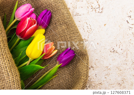 Multicolor tulips bouquet in natural fabric wrapping paper. Spring flowers on the cork background . Top view with place for text. Copy space. Multicolor tulips bouquet in natural fabric wrapping paper. Spring flowers on the cork background . Top view with place for text. Copy space. 127608371