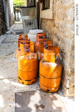 Old gas cylinders stand in a narrow stone alley under the summer sun. Urban infrastructure, fuel storage, and rustic street atmosphere Old gas cylinders stand in a narrow stone alley under the summer sun. Urban infrastructure, fuel storage, and rustic street atmosphere 127608436