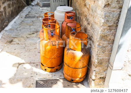 Old gas cylinders stand in a narrow stone alley under the summer sun. Urban infrastructure, fuel storage, and rustic street atmosphere Old gas cylinders stand in a narrow stone alley under the summer sun. Urban infrastructure, fuel storage, and rustic street atmosphere 127608437