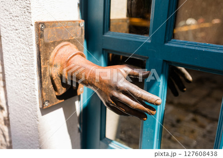 Rusty sculpted hand emerges from a wall beside a blue wooden door. Artistic urban decor, surreal visual element, and unique street detail in Budva, Montenegro. 127608438