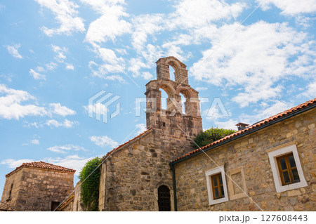 Old stone bell tower under blue sky in Mediterranean village. Historic architecture, cultural heritage and summer travel in Budva, Montenegro. 127608443