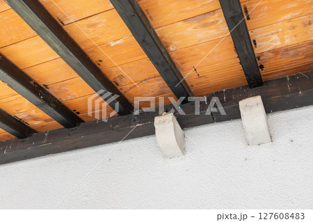 A small bird perches quietly beneath a rustic wooden roof. Architecture detail, natural nesting behavior, and peaceful coexistence in urban environments. 127608483