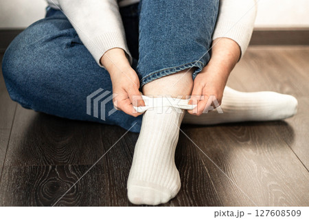 Close-up of young woman putting on fresh white socks while sitting on floor. Perfect for lifestyle, comfort, and daily routine themes 127608509