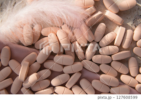 Pills or vitamins on the natural wood background with pink silk fabric and feather in summer day. Top view.  127608599