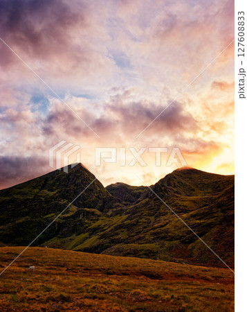 Serene sunset paints the rugged peaks of the Highlands in vibrant hues, casting a warm glow on the tranquil valley below. A solitary sheep grazes peacefully. Serene sunset paints the rugged peaks of the Highlands in vibrant hues, casting a warm glow on the tranquil valley below. A solitary sheep grazes peacefully. 127608833