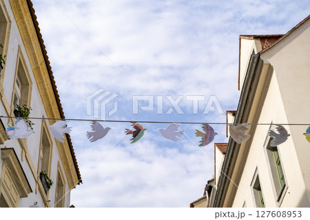 Colorful Paper Birds Gracefully Hanging Between Buildings Beneath a Bright Blue Sky Space 127608953