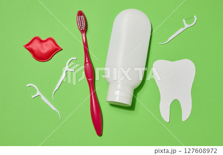 Red toothbrush, white tube of toothpaste, red decorative lips, plastic dental floss holders and white paper tooth cut out on green background. 127608972
