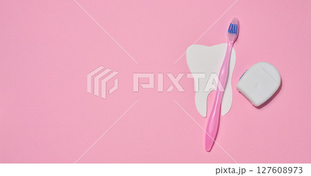 Pink toothbrush, dental floss in a case and a paper cutout tooth placed on a pink background. 127608973