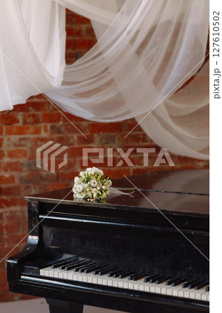 Wedding rings and white rose bouquet on black piano in rustic room with brick wall 127610502