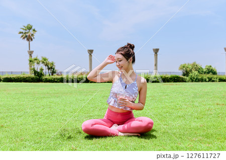 青空の天然芝でヨガ後に水分補給をする健康的な女性 127611727