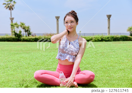 青空の下、天然芝で水分補給するヨガウェアの女性 127611745