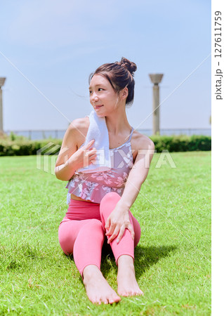 青空の下、天然芝で汗を拭くヨガウェアの女性 青空の下、天然芝で汗を拭くヨガウェアの女性 127611759