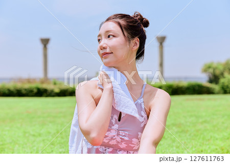 青空の下、天然芝で汗を拭くヨガウェアの女性 青空の下、天然芝で汗を拭くヨガウェアの女性 127611763