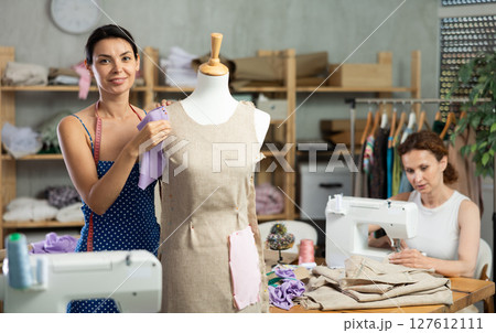 Woman tailor connects parts of dress on mannequin, female craftsman tailor work and sewing Woman tailor connects parts of dress on mannequin, female craftsman tailor work and sewing 127612111