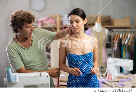 Man tailor takes measurements from female client Man tailor takes measurements from female client 127612114
