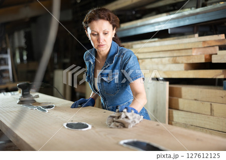 During manufacturing, woman employee grinds surface of wooden board, gives smoothness to surface 127612125