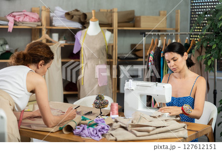 Woman seamstress sewing on a sewing machine. Female tailor drawing dress sketches on paper Woman seamstress sewing on a sewing machine. Female tailor drawing dress sketches on paper 127612151