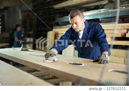 Young man wipes oak plank in workshop Young man wipes oak plank in workshop 127612211