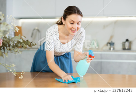 Positive middle-aged woman cleaning the surface of kitchen table 127612245