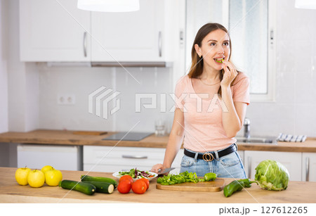 Woman tasting vegetable while cooking salad at home Woman tasting vegetable while cooking salad at home 127612265