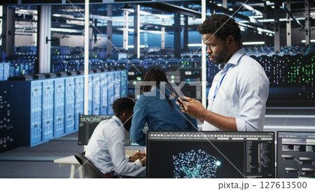 Data center engineer using tablet to interpret AI generated data analytics graphs. Server room worker using artificial intelligence displaying system performance predictive metrics, camera A Data center engineer using tablet to interpret AI generated data analytics graphs. Server room worker using artificial intelligence displaying system performance predictive metrics, camera A 127613500