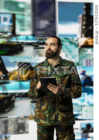 Young soldier working in command center with satellite surveillance integrating data, intelligence and AI warfare tactics for war planning in a national defense mission. Armed forces. 127613508