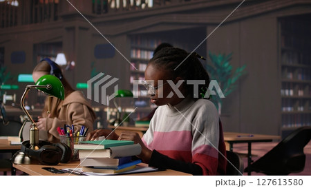 Person waking up african american girl in the university campus library, student falling asleep on stack of borrowed books. Tired and overwhelmed pupil tries to study all night. Camera B. 127613580