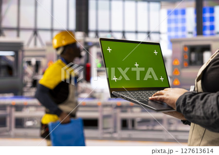 Industry 4.0 expert holding laptop with isolated chromakey template in smart manufacturing plant. The automated factory uses digital interfaces, robotic arms and advanced assembly line. 127613614