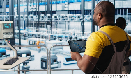 Photovoltaic smart factory engineer uses tablet to design production lines for assembly facility in CAD program. Industry 4.0 solar panels plant worker uses device to optimize floor layouts, camera A Photovoltaic smart factory engineer uses tablet to design production lines for assembly facility in CAD program. Industry 4.0 solar panels plant worker uses device to optimize floor layouts, camera A 127613653