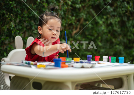 happy toddler girl painting watercolor in paper at backyard. happy toddler girl painting watercolor in paper at backyard. 127617750