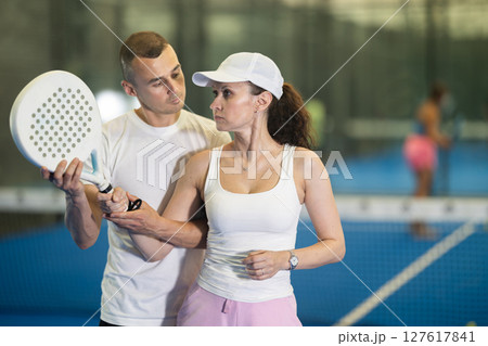 Male trainer teaches woman to play padel and hold racket correctly to hit ball 127617841