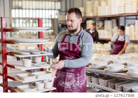 Young man posing at rack with ceramic dishes Young man posing at rack with ceramic dishes 127617886