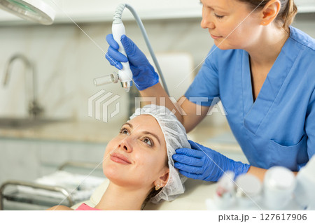Adult woman cosmetologist doing moisturizing procedure to young woman 127617906