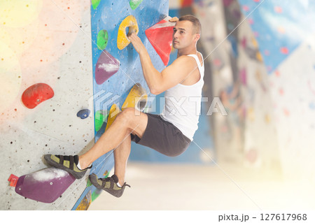 Young man climbing on artificial rock wall in rock-climbing gym Young man climbing on artificial rock wall in rock-climbing gym 127617968