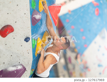 Young man climbing on artificial rock wall in rock-climbing gym Young man climbing on artificial rock wall in rock-climbing gym 127617969