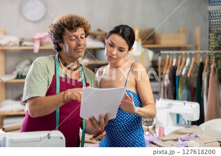 Male tailor shows paper sketch of dress to woman client, Male tailor shows paper sketch of dress to woman client, 127618200