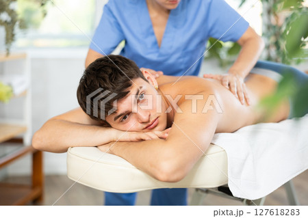 Masseuse doing back massage to young guy 127618283