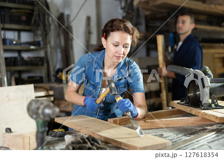 Adult woman works with chisel on oak plank Adult woman works with chisel on oak plank 127618354