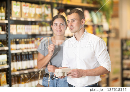 Man with package of eggs in hands talks with wife about buying ingredients for making homemade pie. Man with package of eggs in hands talks with wife about buying ingredients for making homemade pie. 127618355