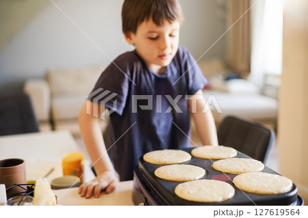 Curious boy watching pancakes cook on griddle in kitchen during morning breakfast preparation moment 127619564