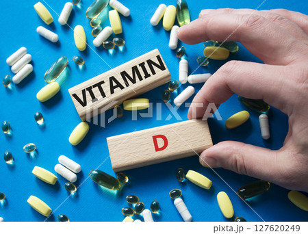 Vitamin D symbol. Concept word Vitamin D on wooden blocks. Beautiful blue background with pills. Doctor hand. Medicine and Vitamin D concept. Copy space Vitamin D symbol. Concept word Vitamin D on wooden blocks. Beautiful blue background with pills. Doctor hand. Medicine and Vitamin D concept. Copy space 127620249