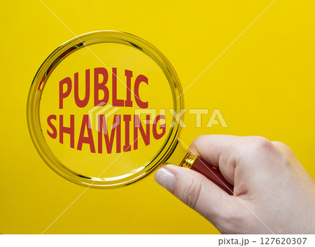 Public Shaming symbol. Magnifying glass with words Public Shaming. Beautiful yellow background. Businessman hand. Business and Public Shaming concept. Copy space. 127620307