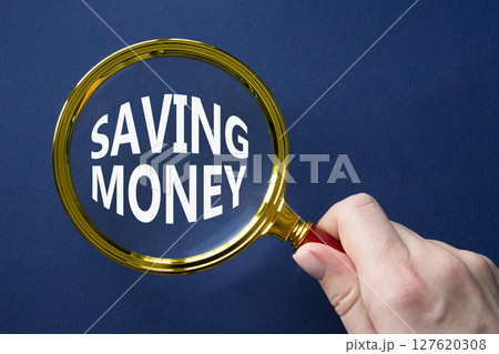 Saving Money symbol. Concept words Saving Money on magnifying glass. Businessman hand. Beautiful deep blue background. Business and Saving Money concept. Copy space. 127620308